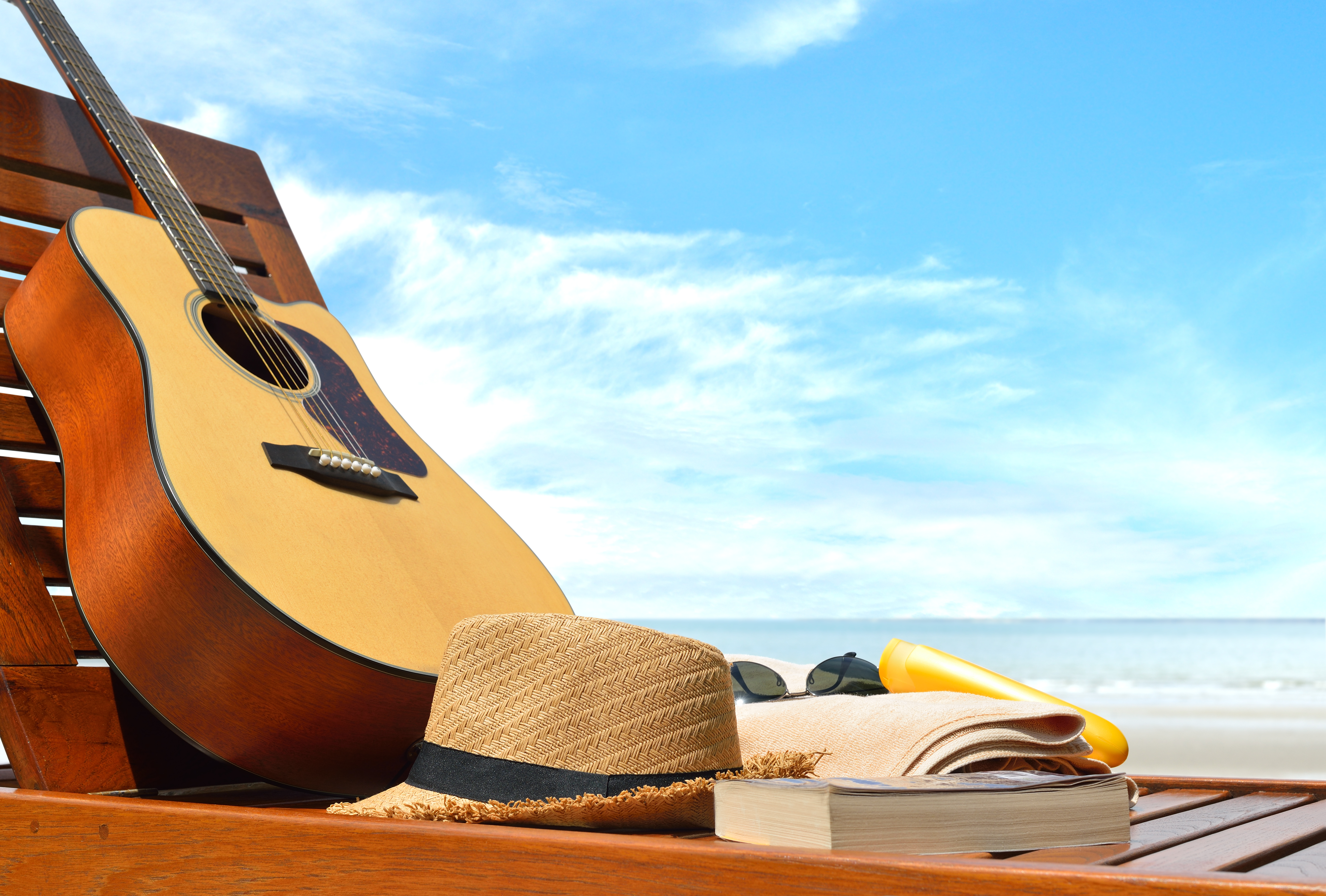 Gitarre, Sonnenhut, Sonnenbrille auf einer Liege am Strand