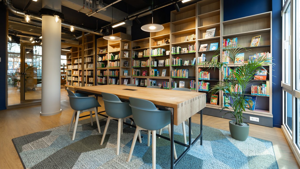 Das Lernstudio Das Lernstudio ist ein Raum mit Bücherregalen an den Wänden und einem Tisch in der Mitte. Pflanzen, ein Teppich und Pendelleuchten machen das Lernstudio wohnlich