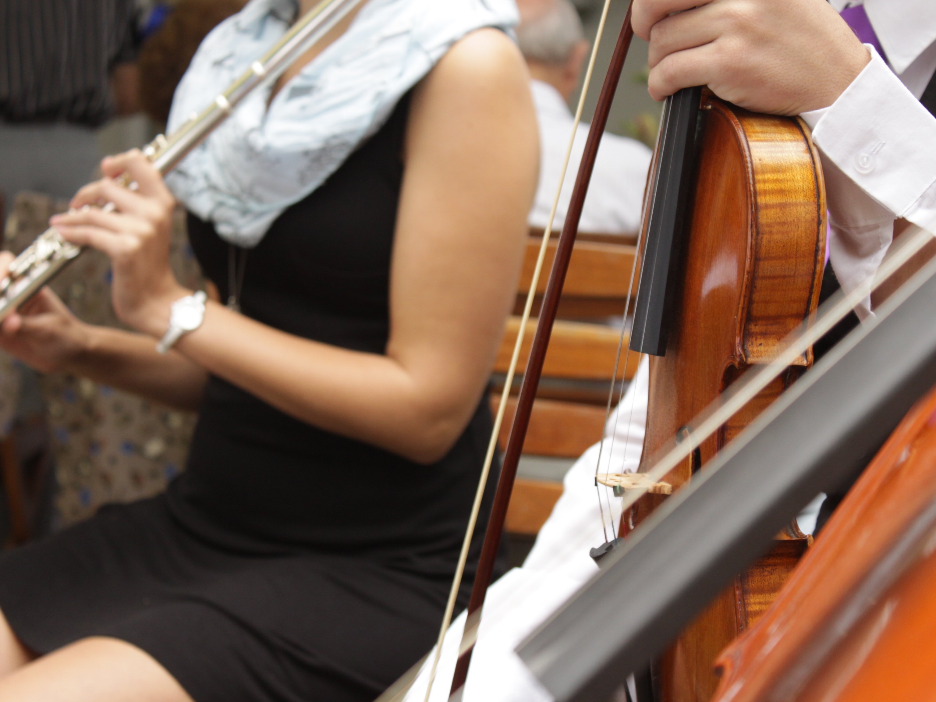 Frau hält Querflöte, weitere Personen mit Violine und Cello