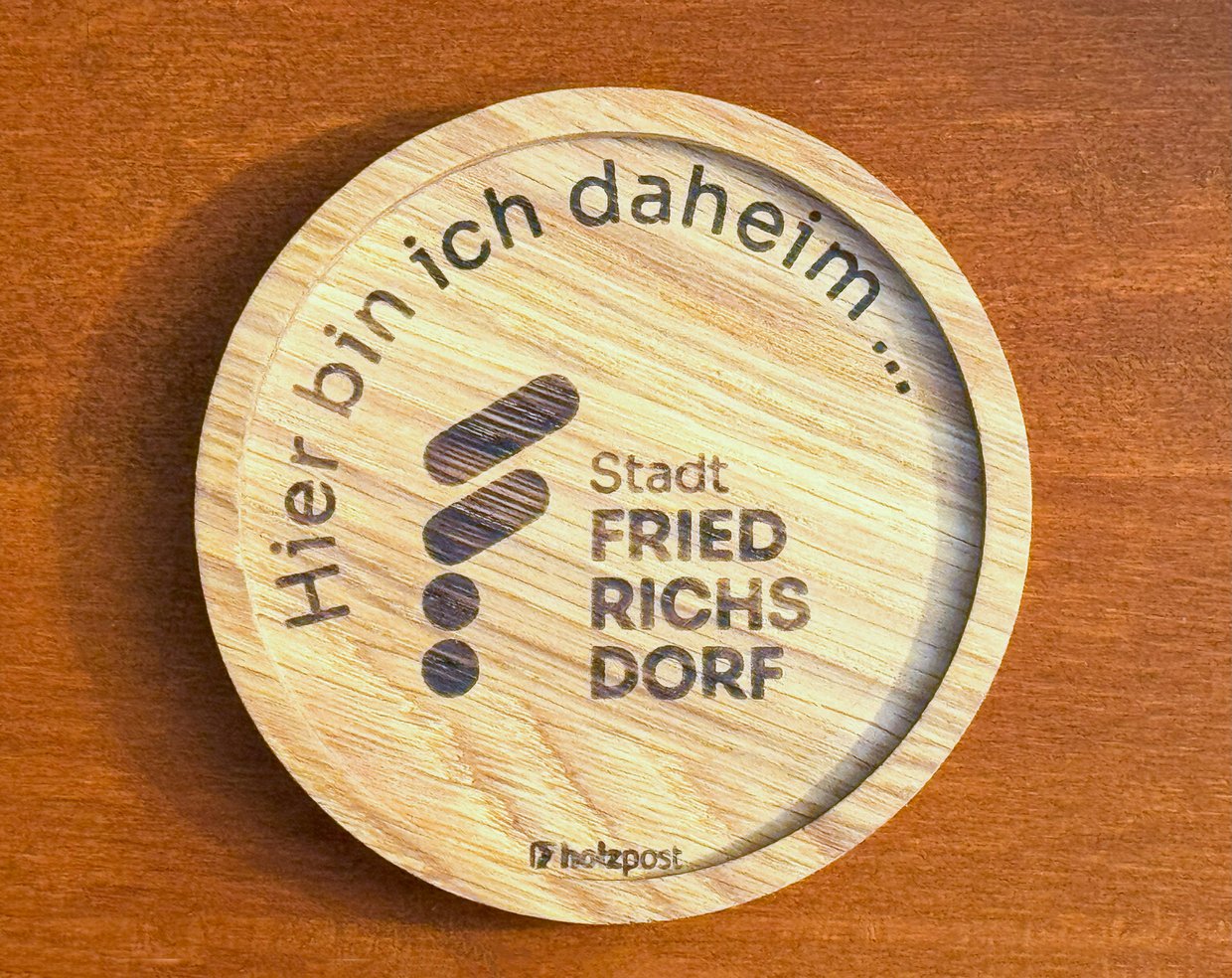 Auf dem Bild ist ein Holzuntersetzer mit dem Logo der Stadt Friedrichsdorf zu sehen.
