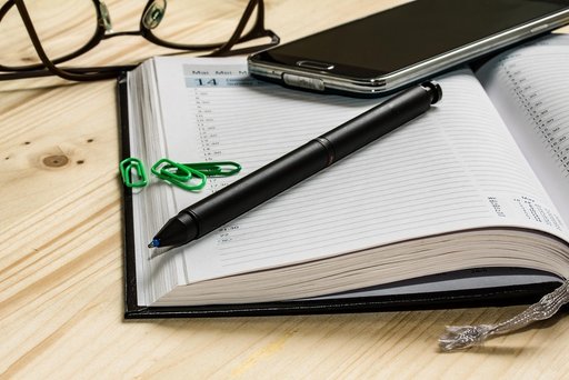 Kalender mit Stift, Brille, Handy und Büroklammern auf Tisch