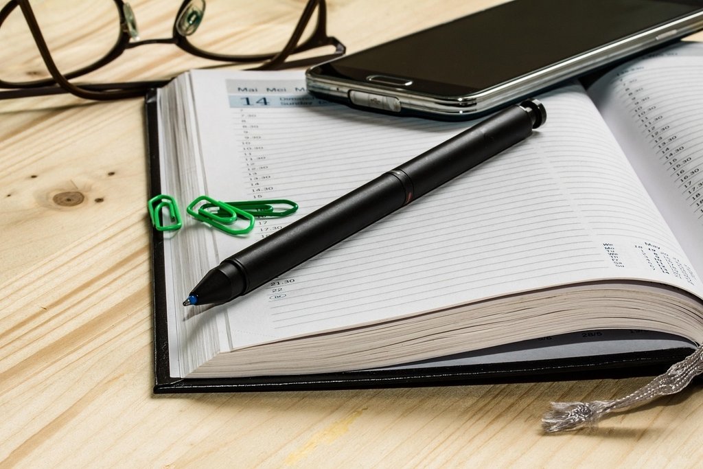 Kalender mit Stift, Brille, Handy und Büroklammern auf Tisch