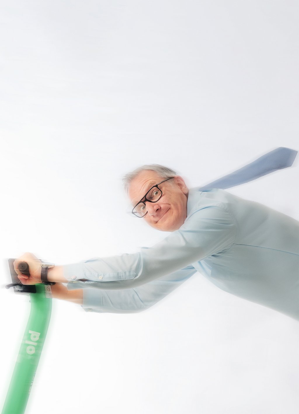 Auf dem Bild ist Hans Gerzlich mit fliegender Krawatte zu sehen, wie er rasant auf einem E-Roller fährt.