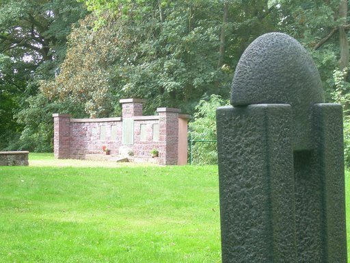 Gefallenendenkmal auf dem Friedhof in Burgholzhausen: Gemauerte Wand, in die sieben Gedenkplatten eingefügt sind. Vor der Wand sind eine Löwenfigur und ein Inschriftenstein angebracht. Im Vordergrund ist noch die Rückseite eines Grabmals zu sehen.