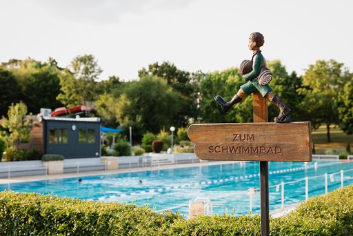 Hinweisschild: Junge mit Badesachen unterm Arm, der Richtung Schwimmbad spaziert