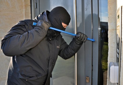 Mann mit Maske und Einbruchswerkzeug an Eingangstür