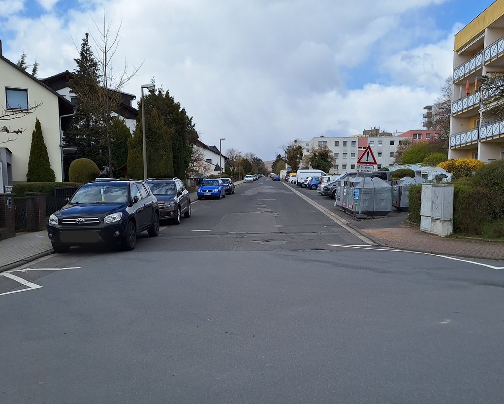 Das Bild zeigt einen Blick in die Ostpreußenstraße von der Berliner Straße zur Danziger Straße/Stettiner Ring. In Straßenmitte sind deutliche Straßenschäden sichtbar, links und rechts stehen parkende Fahrzeuge