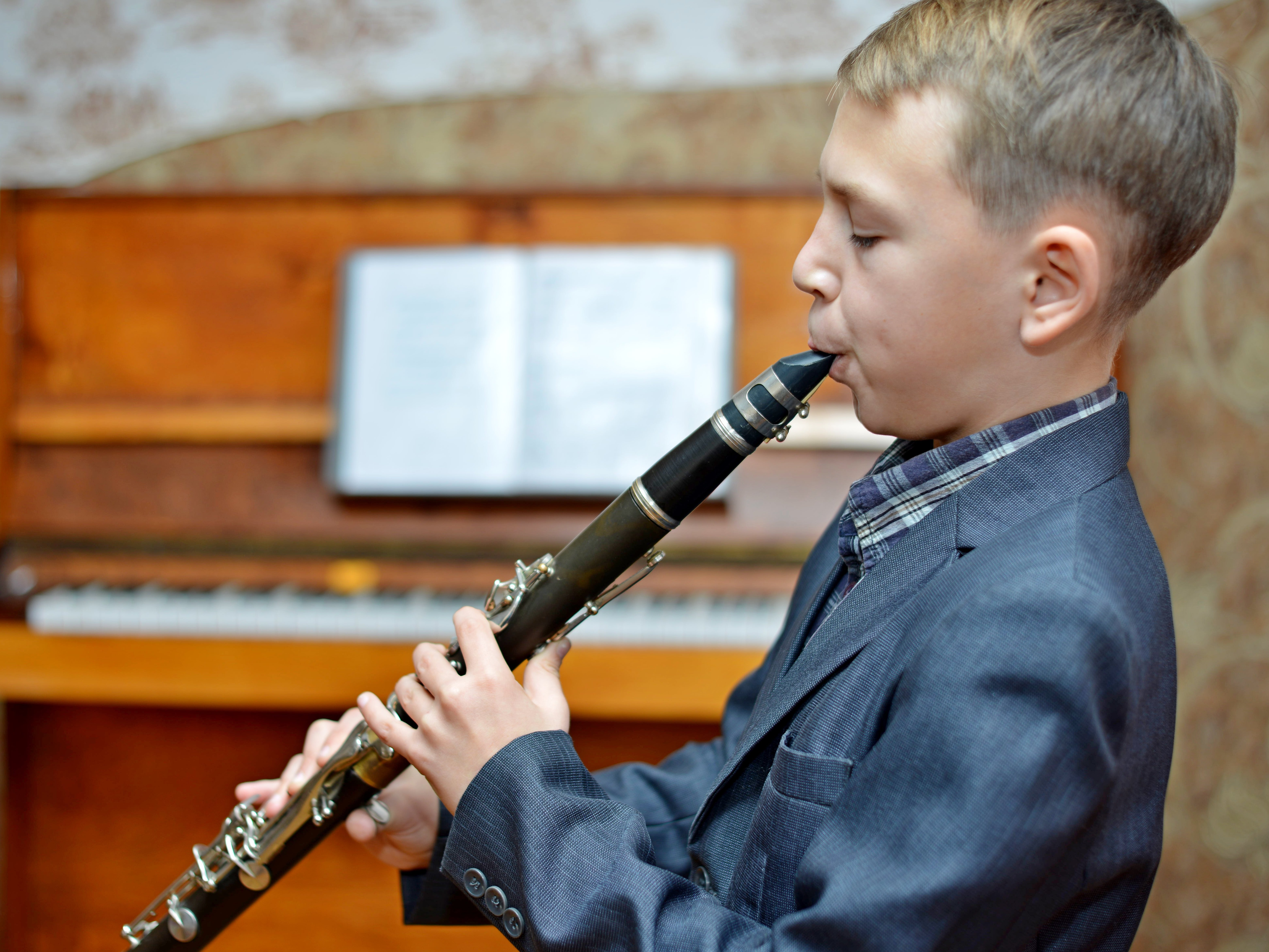 Kleiner Junge spielt Klarinette, ein Klavier steht im Hintergrund
