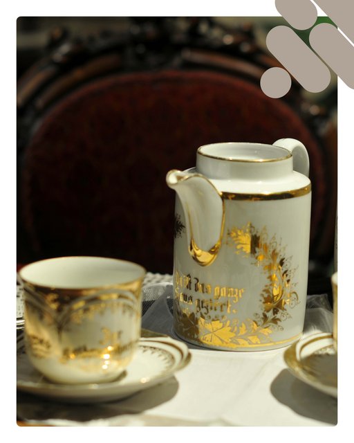 Zu sehen ist ein altes Porzellangeschirr. Mit Goldenen Blätterranken verziert. Auf Kaffeekanne und Milchkännchen steht eine schlecht erkennbare Schrift. Die beiden Tassen und die Kannen stehen auf einem Spitzentuch, auch einem alten Holztisch. Im Hintergrund sieht man einen alten Holzstuhl.