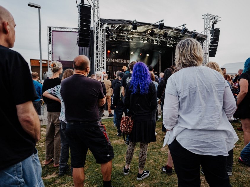 Das Foto zeigt Menschen, die vor der Bühne im Sportpark stehen und der Musik zuhören. 