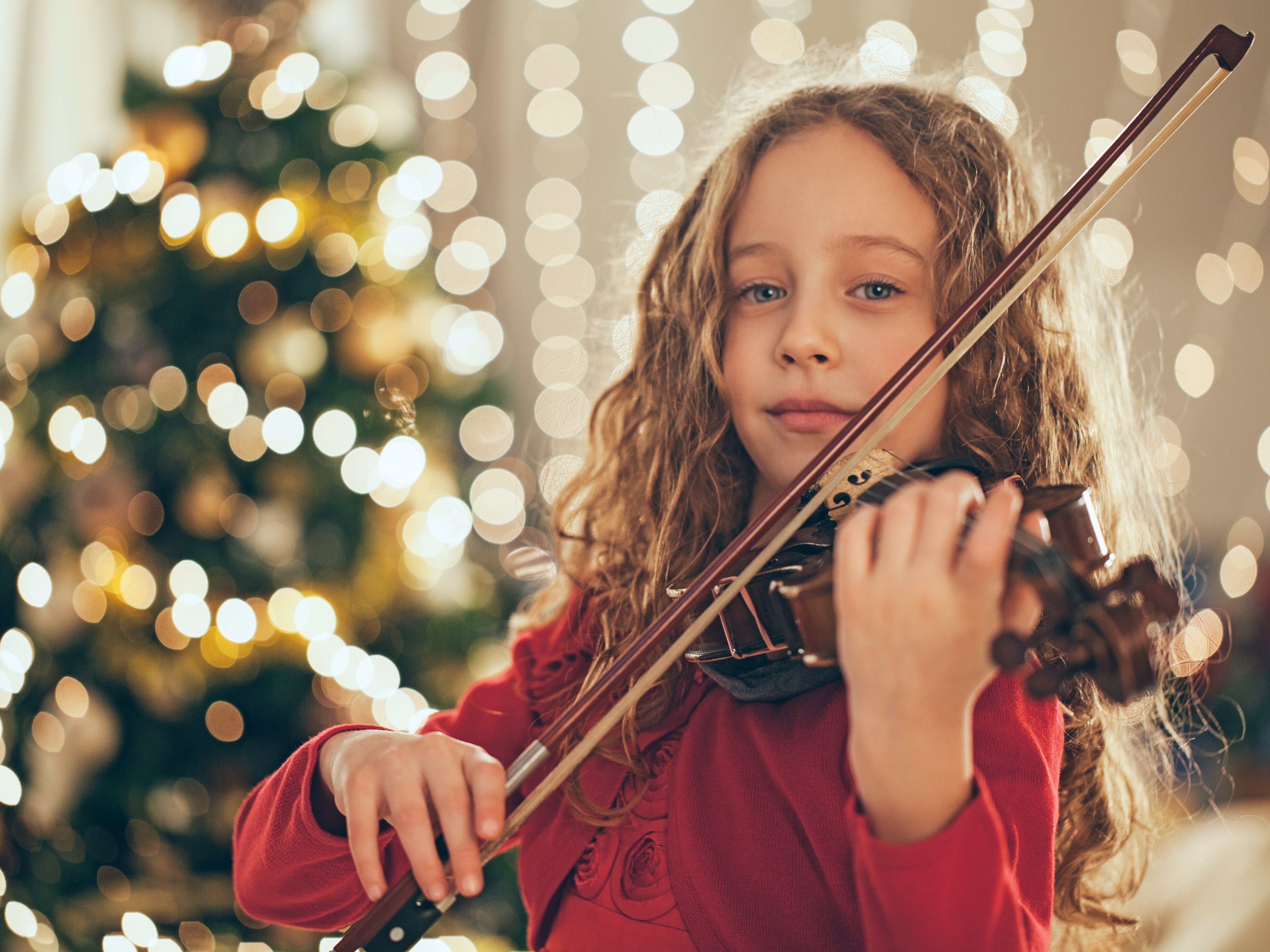 Junges Mädchen hält Geige, im Hintergrund ein Weihnachtsbaum