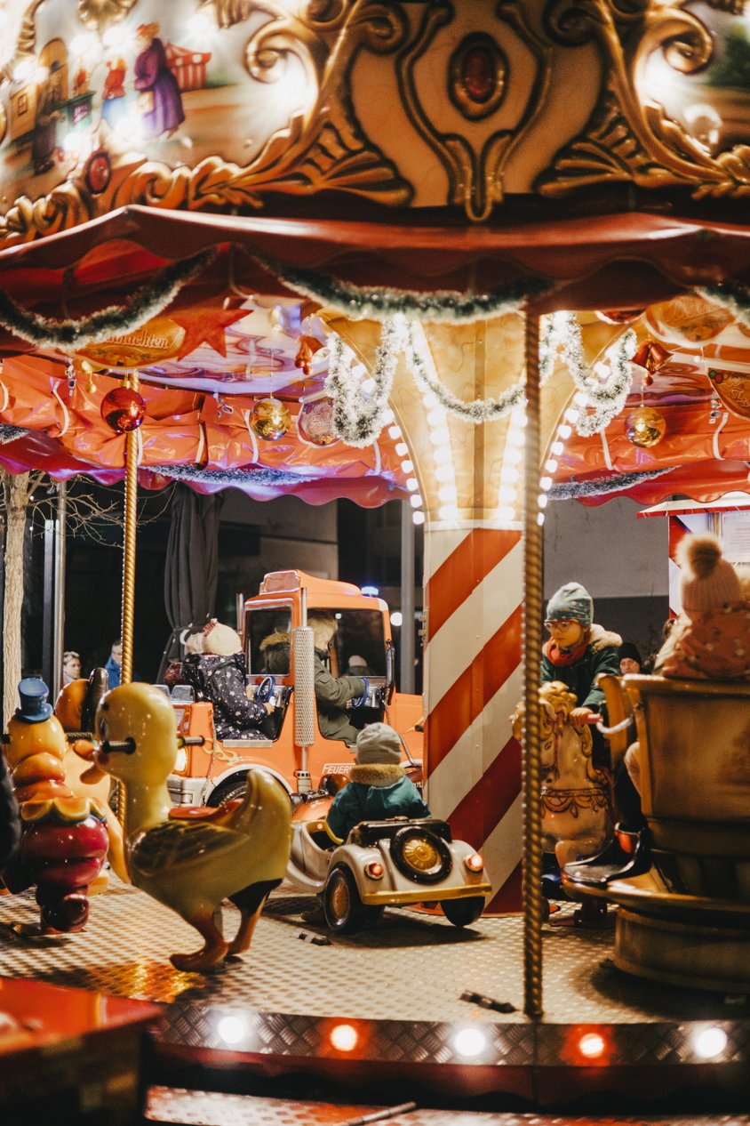 Ein Kinder Karussell auf dem einige Kinder sitzen. Es ist dunkel und das Karussell ist hell erleuchtet. 