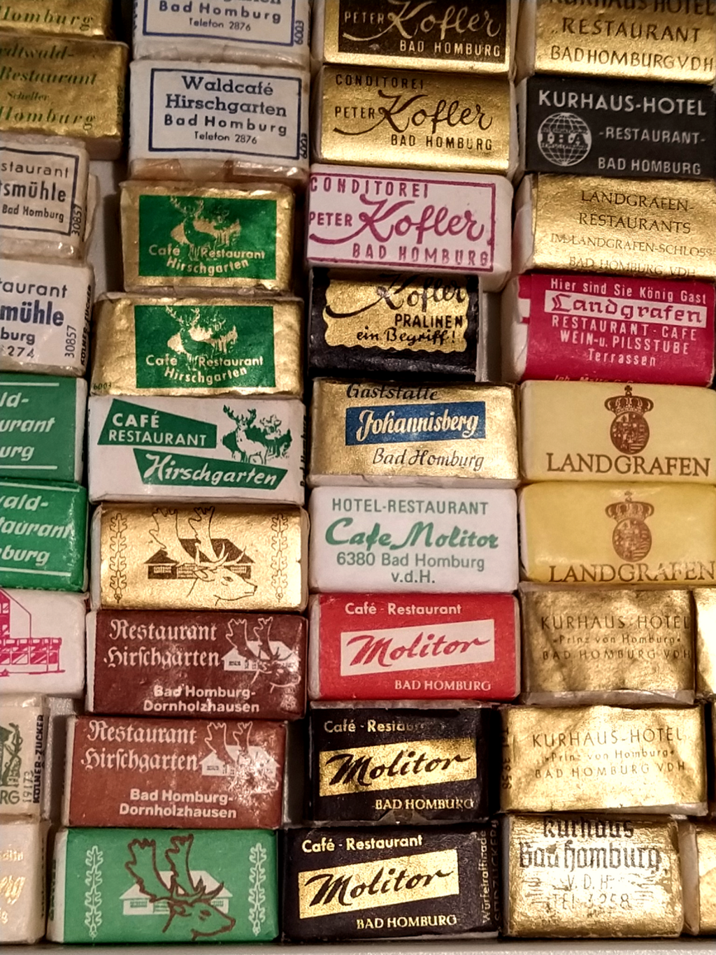Nahaufnahme einer Sammlung nostalgischer, einzeln verpackter Zuckerwürfel mit historischen Werbeaufdrucken verschiedener Cafés und Restaurants, zum großen Teil aus Bad Homburg.