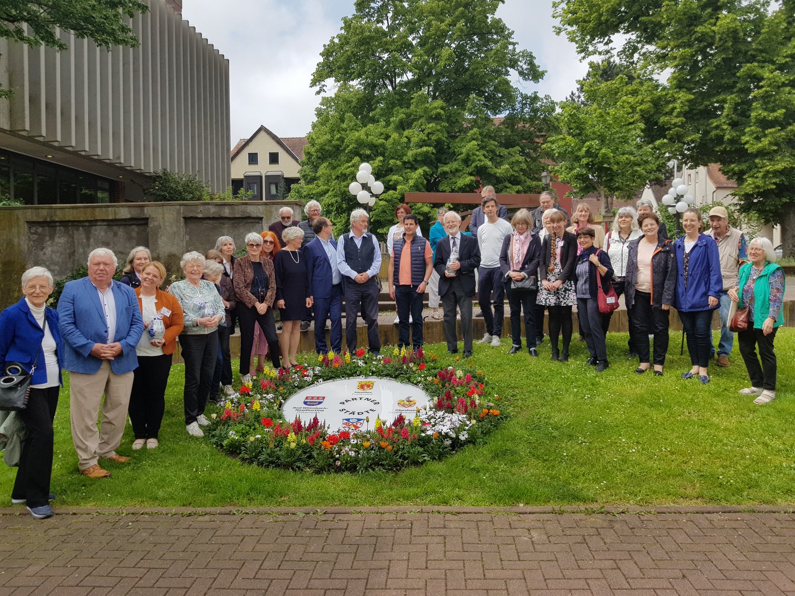 Auf der Darstellung sind die Gäste des Pfingsttreffens zu sehen, die das mit Blumen umpflanzte Schild aller Wappen umrahmen. 