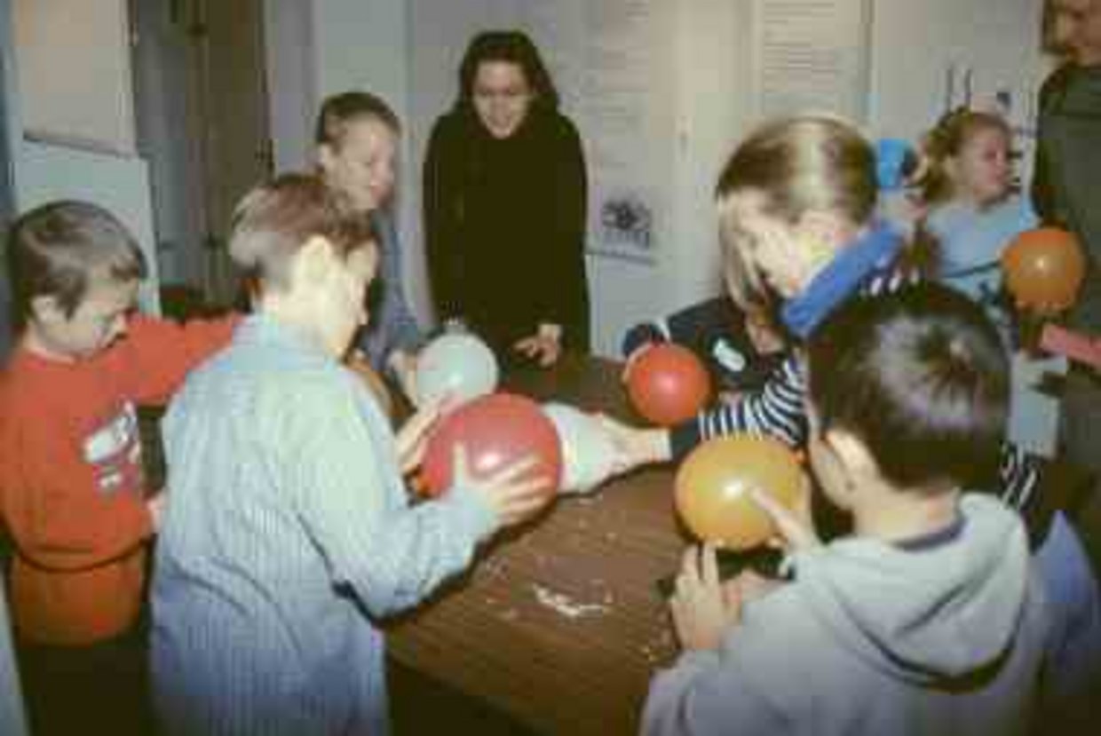 Kinder und Erwachsene stehen um einen Tisch herum und experimentieren mit einem Luftballon