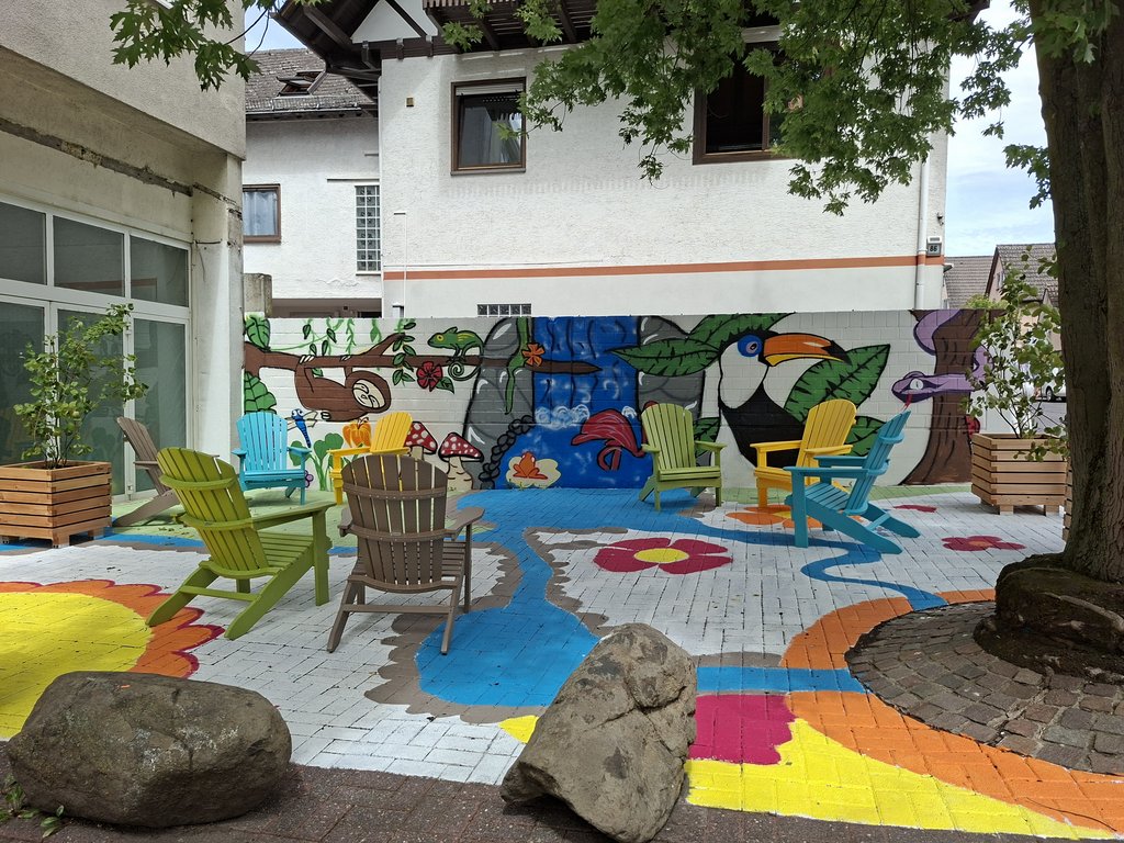 Bunt gestaltete Stadtterasse mit Sesseln, Bäumchen und fabenfrohen Wänden zum Verweilen für alle.