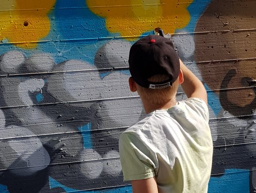Auf dem Bild ist ein Jugendlicher zu sehen, der mit Farbe ein Graffiti an eine Wand sprüht.