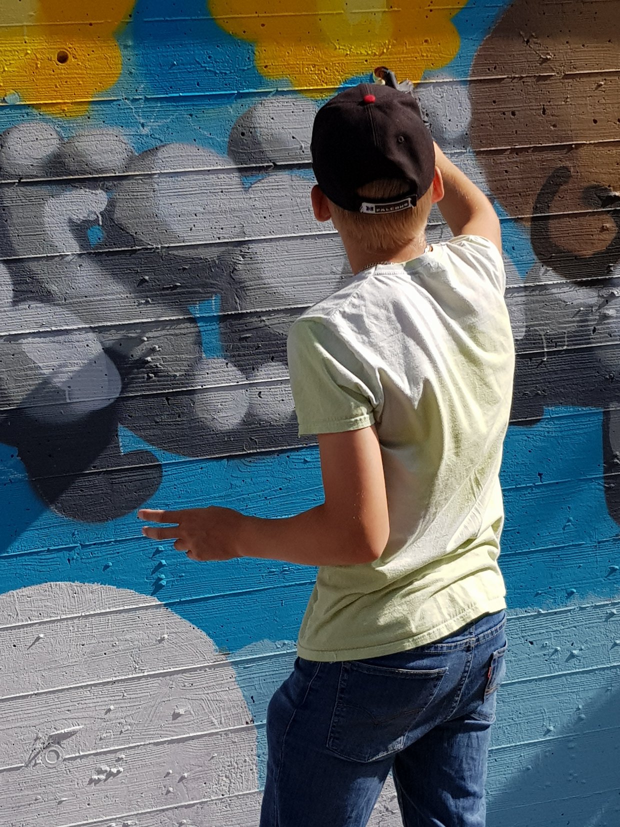 Auf dem Bild ist ein Jugendlicher zu sehen, der mit Farbe ein Graffiti an eine Wand sprüht.