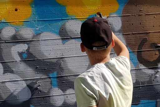 Auf dem Bild ist ein Jugendlicher zu sehen, der mit Farbe ein Graffiti an eine Wand sprüht.