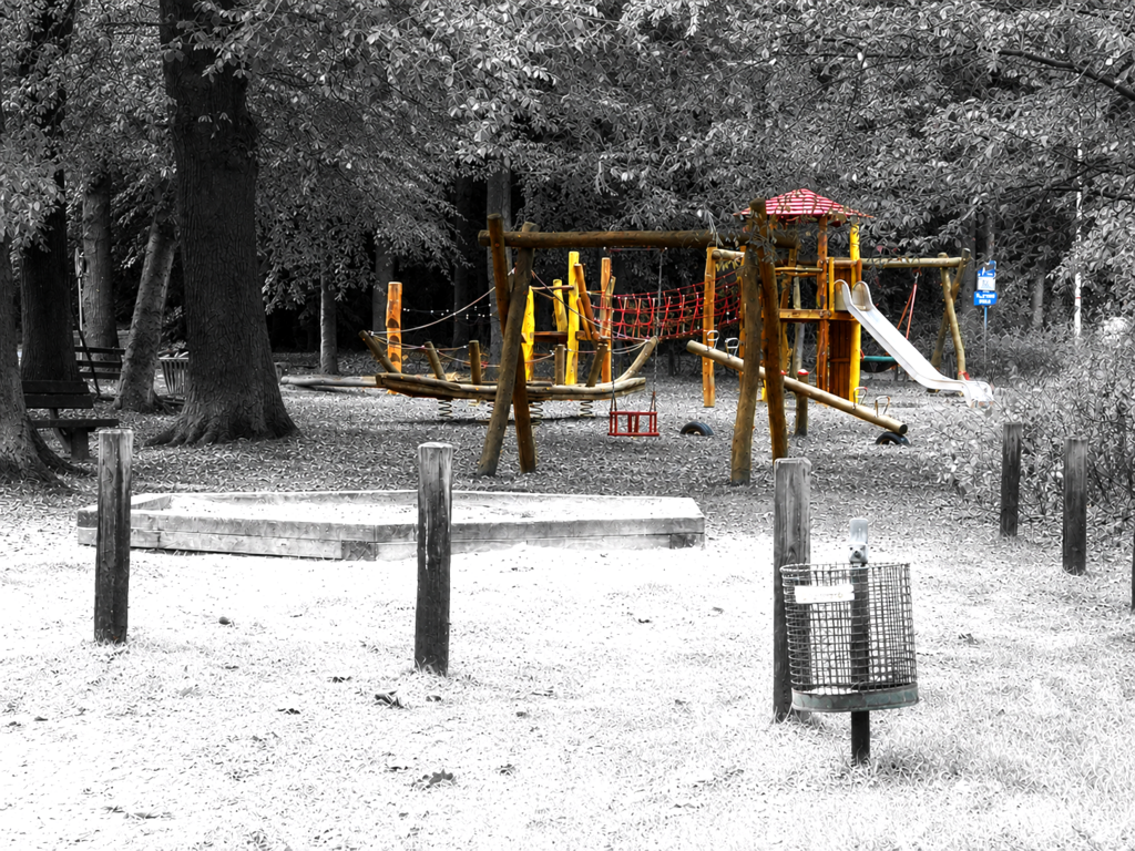 Ein Spielplatz mit großem Sandkasten. Alles grau - nur die Spielgeräte sind farbig.