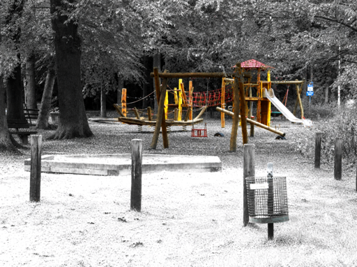 Ein Spielplatz mit großem Sandkasten. Alles grau - nur die Spielgeräte sind farbig.