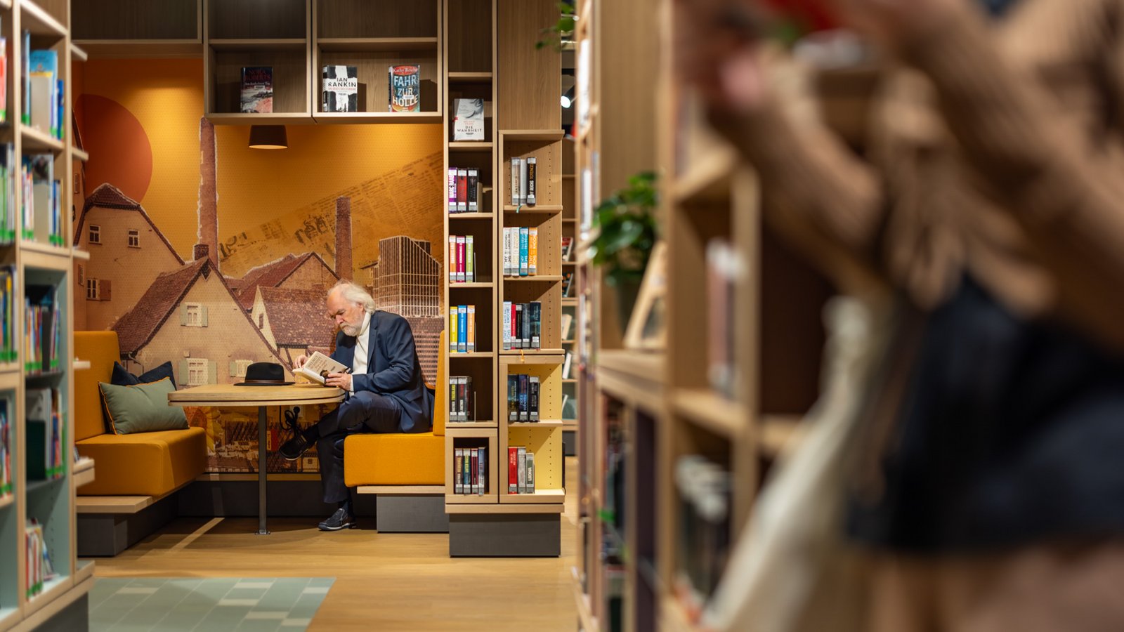 Ein Mann sitzt lesend in einer Kabine. Die Kabine ist mit zwei orangen Sofas und einem Tisch ausgestattet.