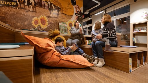 2 Frauen sitzen mit 2 Kindern auf den Stufen und im Sitzsack in der Kinderbücherei. 