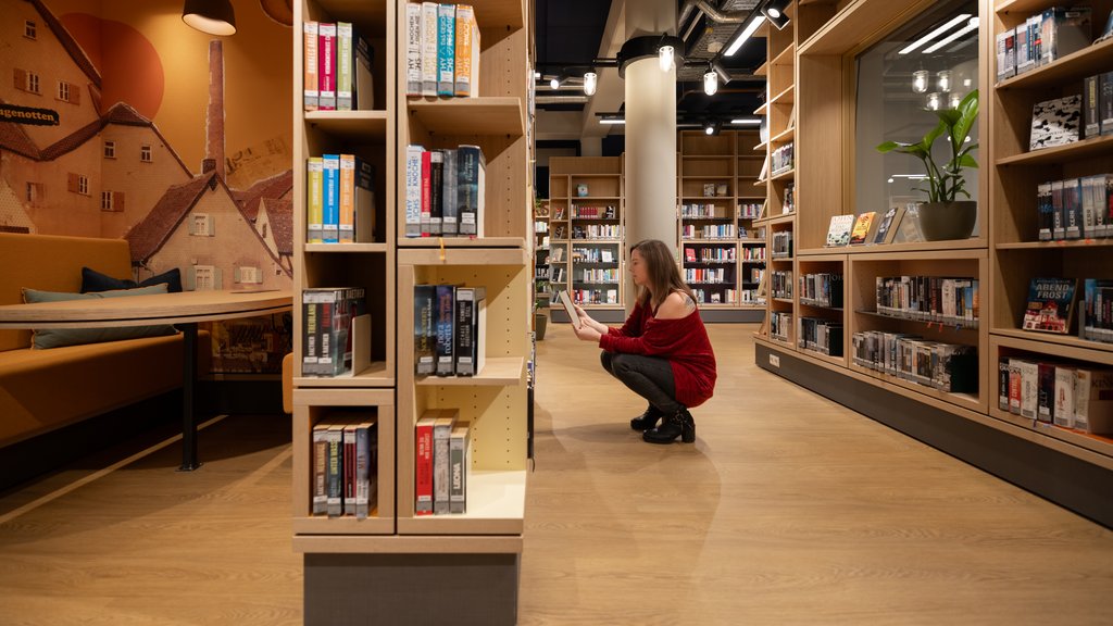 Eine Frau kniet in der Stadtbücherei vor einem Bücherregal und schaut sich ein Buch an.