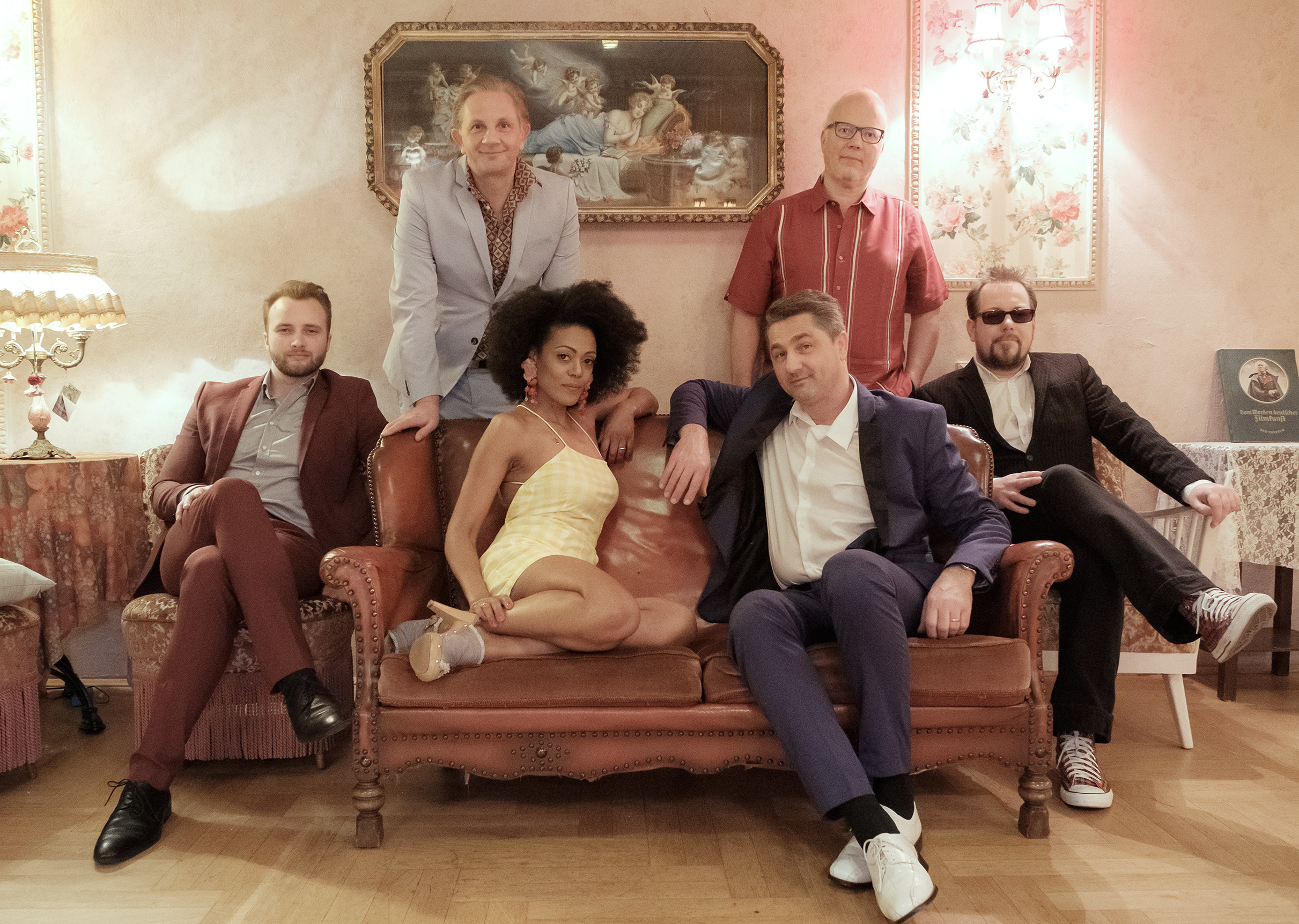 Auf dem Bild ist die sechsköpfige Band auf einem Sofa sitzend und dahinter stehend zu sehen.
