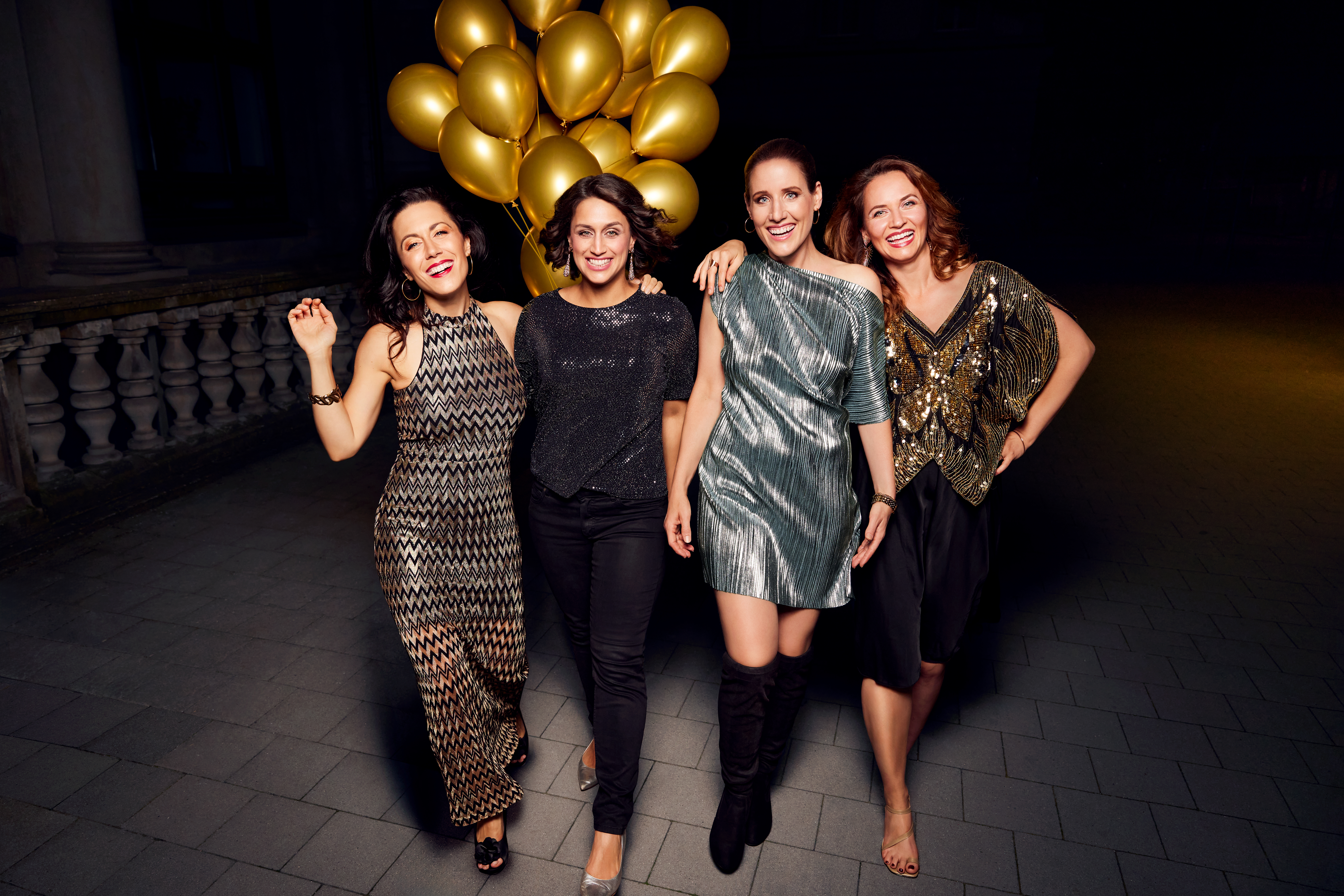 Auf dem Bild sind die vier Sängerinnen in Abendgarderobe zu sehen, im Hintergrund ein großer Strauß goldener Luftballons.