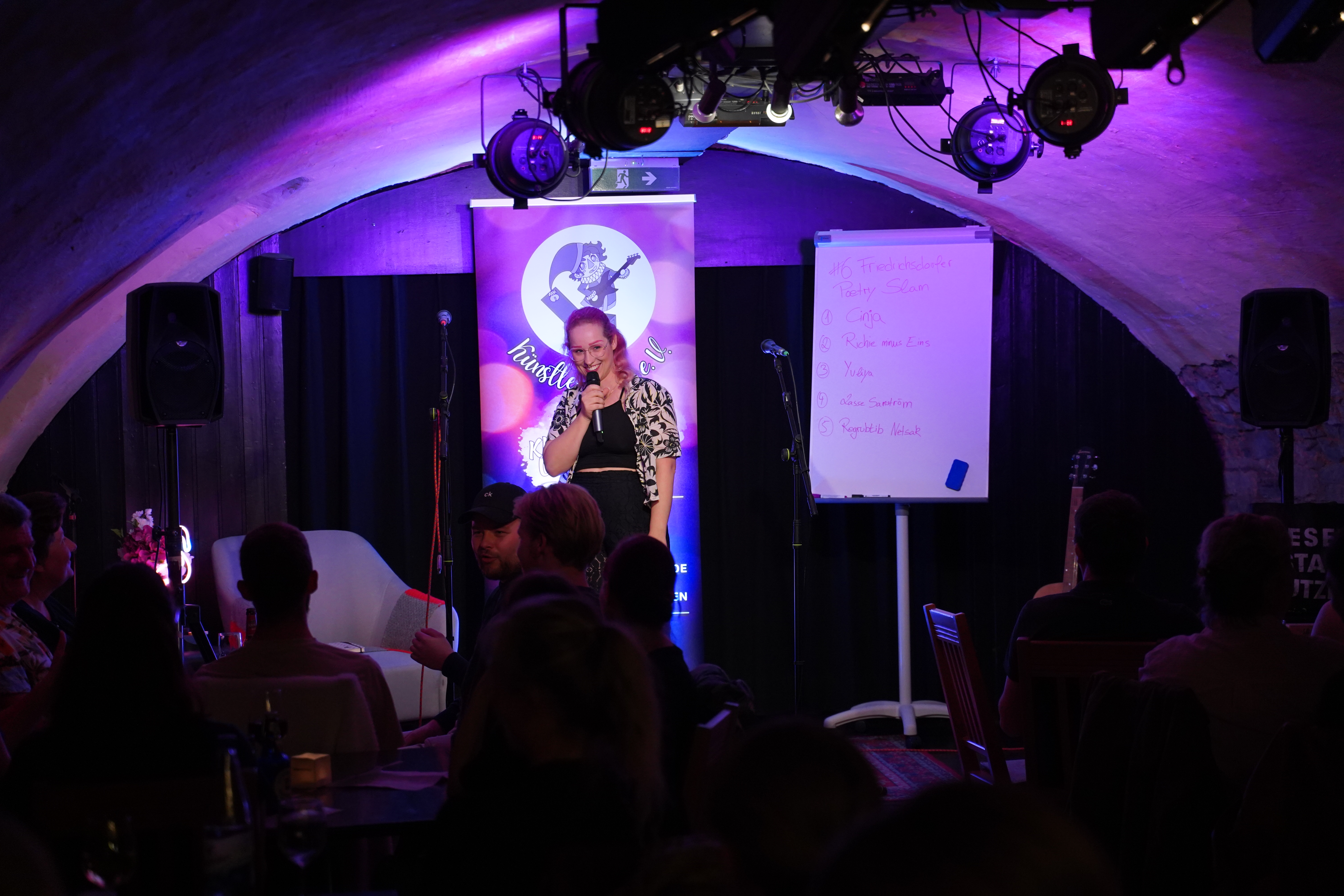 Auf dem Bild ist eine Frau mit Mikrofon auf der Bühne zu sehen.