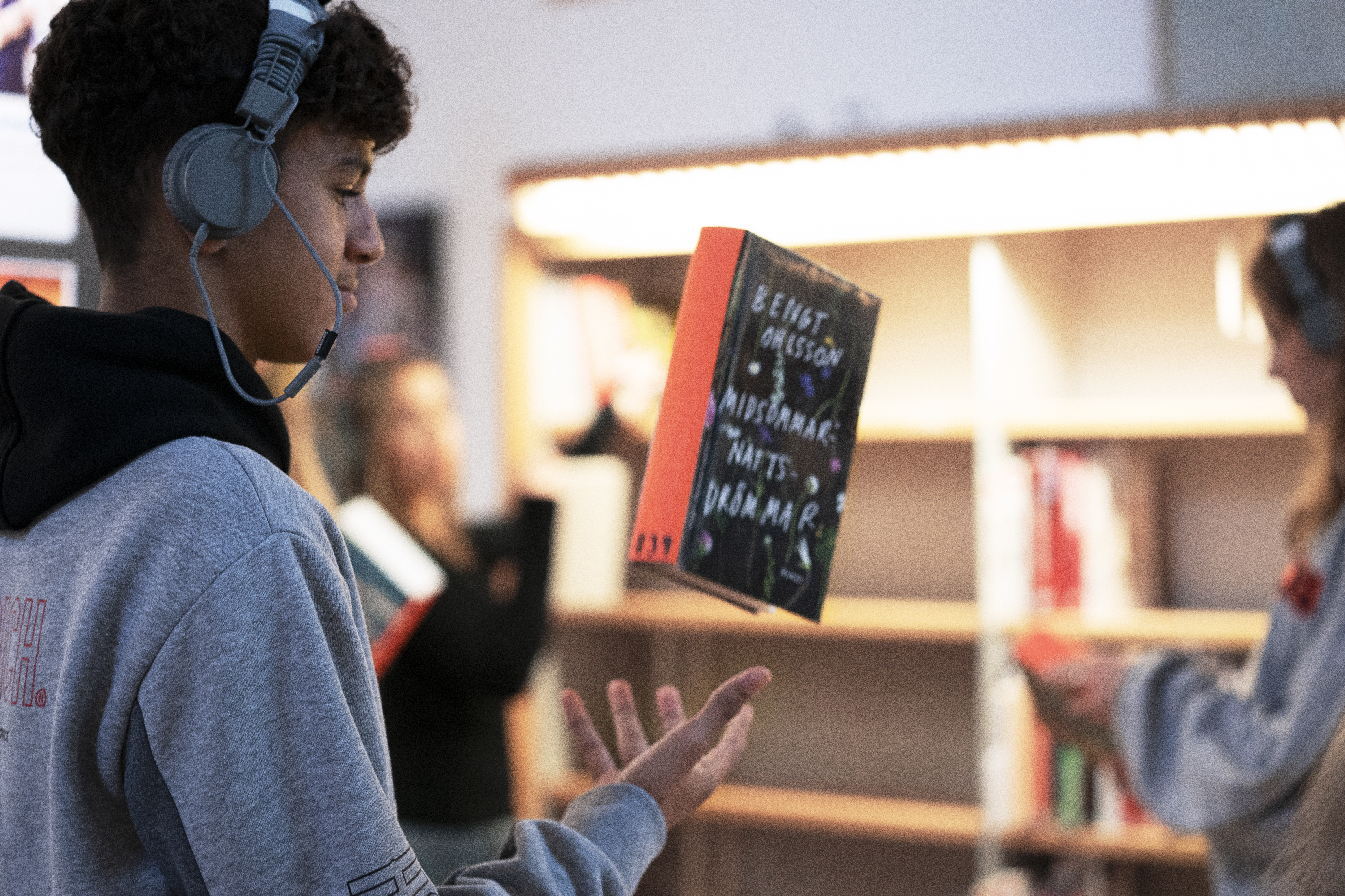 Auf dem Bild ist eine Jugendlicher mit Kopfhörer zu sehen, der ein Buch in die Luft wirft.