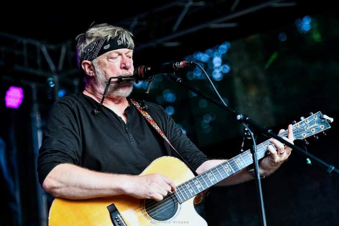 Auf dem Bild ist ein Mann mit Gitarre und Mundharmonika zu sehen.