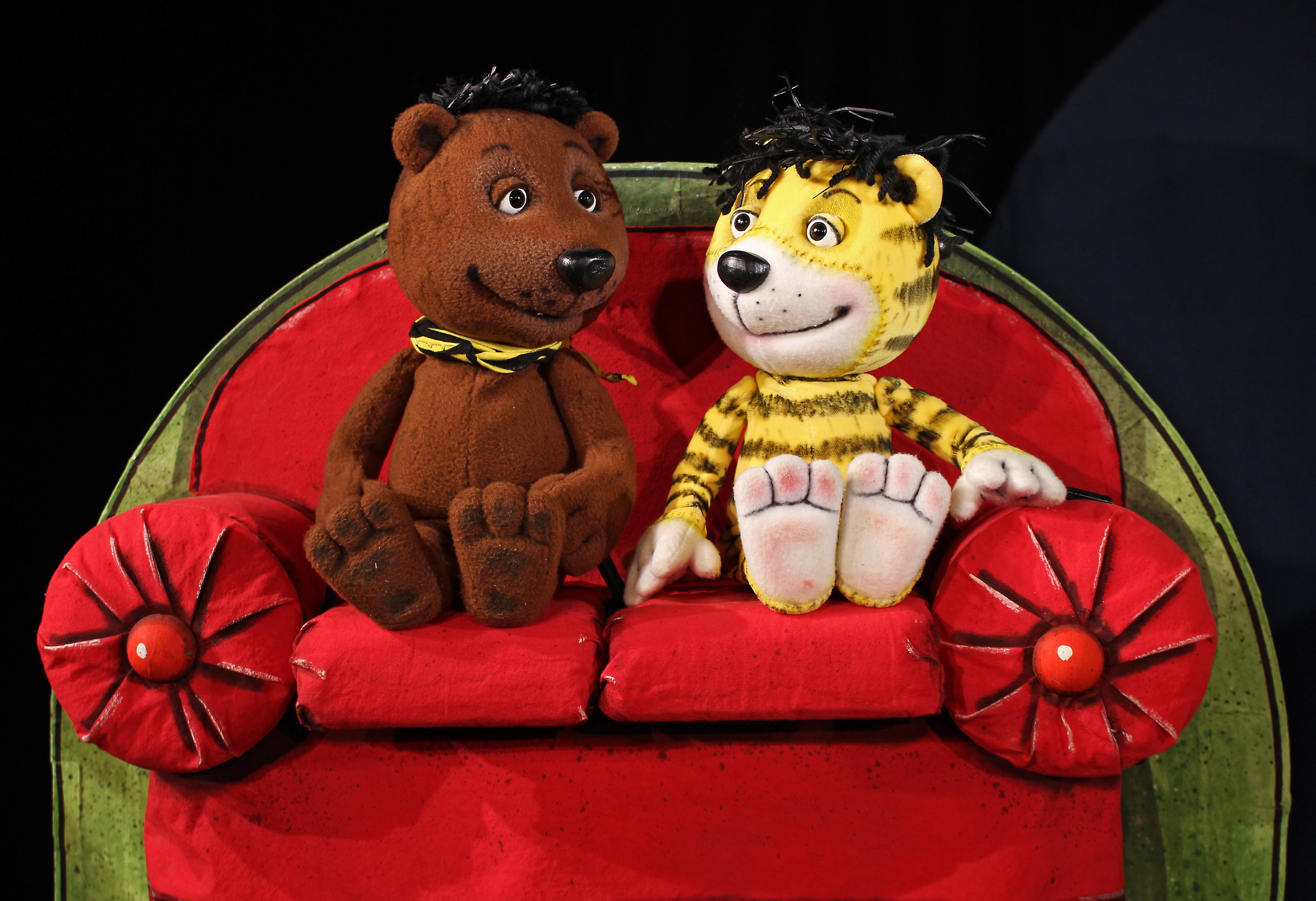 Auf dem Bild sind die Figuren Bär und Tiger auf einem Sofa sitzend zu sehen.