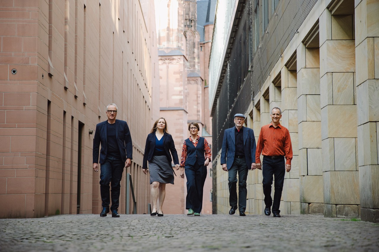 Auf dem Bild sind die fünf Musiker von Pia and the Ambassadors zu sehen, die durch eine Häuserschlucht laufen.