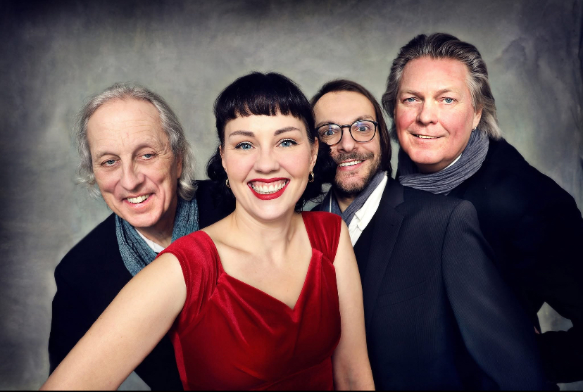 Auf dem Bild ist die Sängerin Anja Tschenisch in rotem Kleid mit ihren drei Musikerkollegen zu sehen.